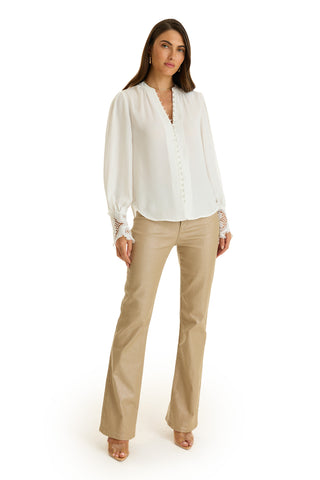 A woman poses against a white background wearing the Blake Lace Sleeve Blouse in white with lace cuffs, paired with beige flare pants and nude open-toe heels.