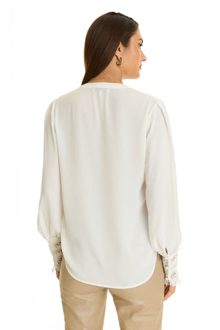 A woman with long brown hair, wearing the Blake Lace Sleeve Blouse in white and tan pants, stands facing away from the camera against a white background.