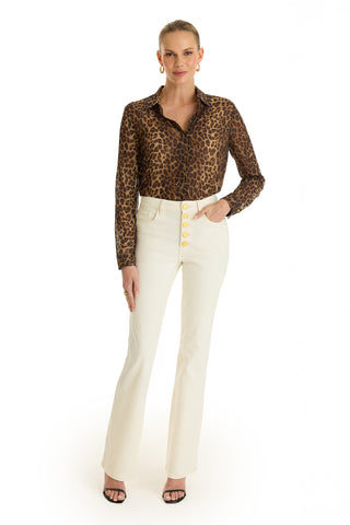 A woman stands facing forward in the Ana Chiffon Blouse - Leopard, paired with high-waisted white pants, black heeled sandals, gold hoop earrings, and a ring, posed against a plain white background.