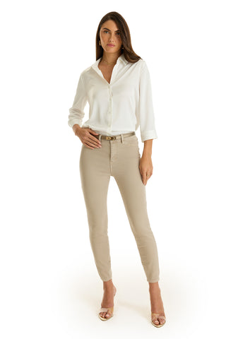 A woman with long brown hair poses confidently against a white background, wearing the Sara Silk Blouse in White, paired with beige fitted pants and nude high-heeled sandals.
