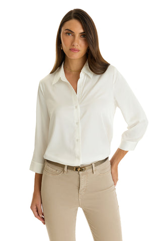 A woman with long brown hair wears the Sara Silk Blouse in white, styled with rolled 3/4 sleeves, beige pants, and a brown belt. She stands against a plain white background, one hand resting on her hip.