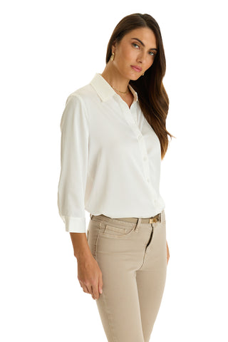 A woman with long brown hair models the Sara Silk Blouse in white, featuring three-quarter sleeves, paired with beige pants. She stands against a white background and gazes slightly to the side.