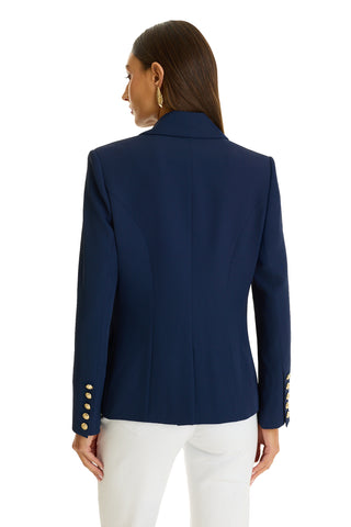 A woman with long brown hair is seen from the back wearing the Sasha Double Breasted Blazer in navy with gold cuff buttons and white pants, set against a white background.