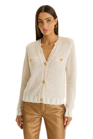 A woman with straight brown hair wears the Shannon Sequin Cardigan Top in Pearl, featuring textured knit, gold dome buttons, and front pockets, paired with tan trousers against a white background.