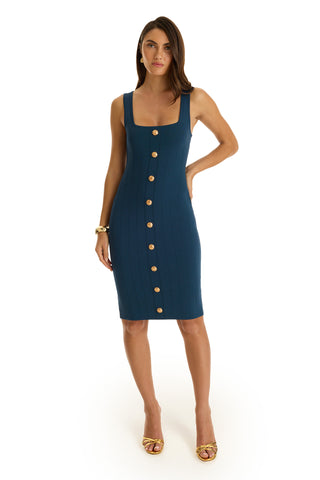 Woman wearing the Helena Button Dress - Ocean, a sculpted knit dress in teal with a square neckline and gold dome buttons. She poses with one hand on her hip, loose hair, and gold sandals against a white background.