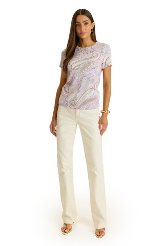 A woman faces forward against a white background, wearing the Amaya Ultra-Soft T-Shirt in pastel paisley, paired with cream straight-leg pants, beige heeled sandals, and gold jewelry.