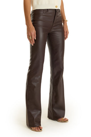 A woman wears the Aria Coated Flare Jean - Espresso, a high-rise, dark brown faux leather pant, styled with a sleeveless light top, rings, bracelet, and open-toe heeled sandals. Only her torso and legs are visible against a plain background.