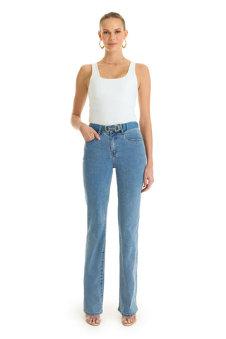 A woman faces forward, wearing the Loren Bodysuit - White, paired with light blue high-waisted jeans, a belt, hoop earrings, and open-toe heels against a white background. One hand is in her pocket.
