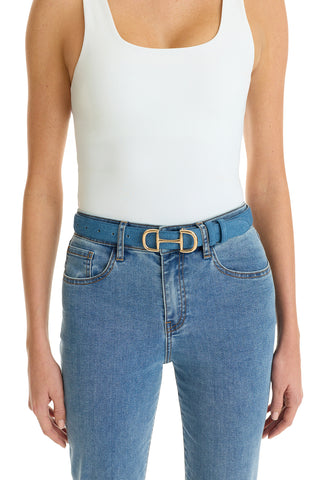 A person wears a white sleeveless top tucked into blue jeans with the Bettie Belt - Denim, which features a gold horsebit buckle. The image is cropped from the shoulders to upper thighs.
