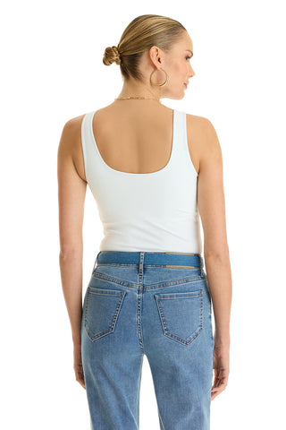 A woman with blonde hair in a bun wears the Loren Bodysuit - White, paired with high-waisted blue jeans. She faces away from the camera, highlighting the back of her outfit, large hoop earrings, and a thin necklace.