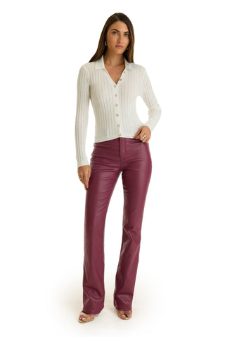 A woman stands facing forward in a white ribbed button-up sweater and Aria Coated Flare Jean in Sangria. She has long, straight brown hair and open-toed heels, posing against a plain white background.