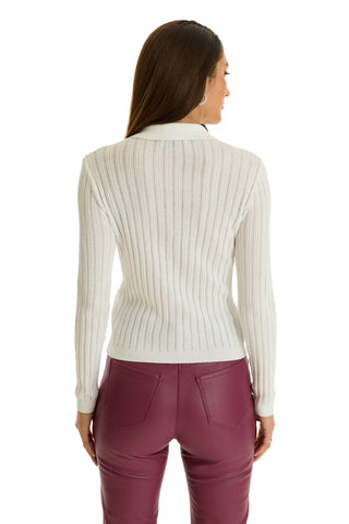 A woman with long brown hair is shown from the back, wearing the Karolina Polo Shirt in white and high-waisted maroon leather pants against a white background.