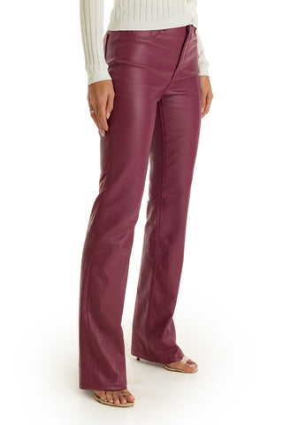 A person wears high-waisted Aria Coated Flare Jean in Sangria with a white ribbed sweater and open-toed heels, standing against a white background.