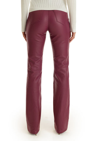 A person wearing Aria Coated Flare Jean in Sangria, a high-rise burgundy leather pant with a flared fit, and a white ribbed sweater, shown from the back against a white background.