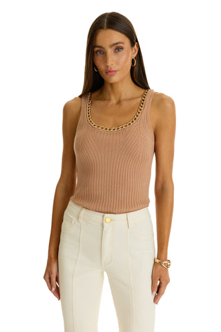 A woman wears the Millie Knit Tank in mocha featuring a gold-toned chain neckline, paired with high-waisted white pants, standing with her arms relaxed at her sides against a plain white background.