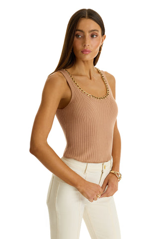 A woman with long brown hair wears the Millie Knit Tank in mocha, featuring a ribbed texture and gold-toned chain neckline, paired with high-waisted white pants. She stands against a white background, looking slightly to the side.