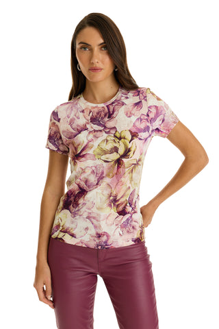 A woman stands with one hand on her hip against a white background, wearing the Amaya Ultra-Soft T-Shirt – French Garden with short sleeves and a floral print in pink, purple, and yellow, paired with burgundy pants.