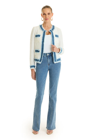 A woman stands against a white background wearing the Julia Tweed Jacket in Denim/White, paired with a white top, blue jeans, hoop earrings, and open-toe heels. Her hair is pulled back and she has one hand in her pocket.