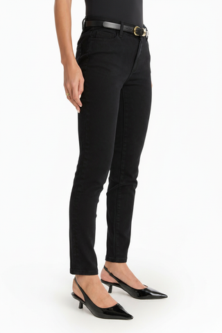 A person wears the Layla Skinny Jean - Black in a figure-hugging fit, paired with a black belt, black top, and black pointed-toe heels. The photo shows the outfit from the waist down against a white background.