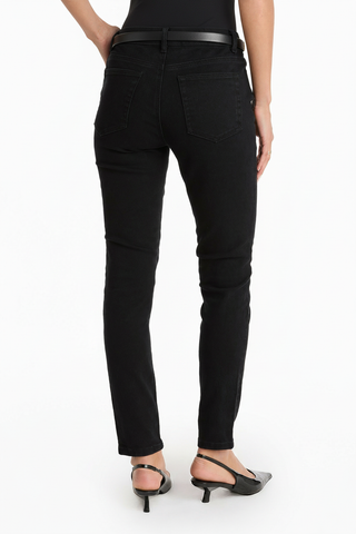 A person stands facing away against a plain white background, wearing the Layla Skinny Jean - Black, styled with a black belt and black heeled sandals for a figure-hugging look.