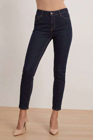 Wearing the Layla Skinny Jean - Indigo and nude high heels, a person stands on a wooden floor against a plain light-colored background.