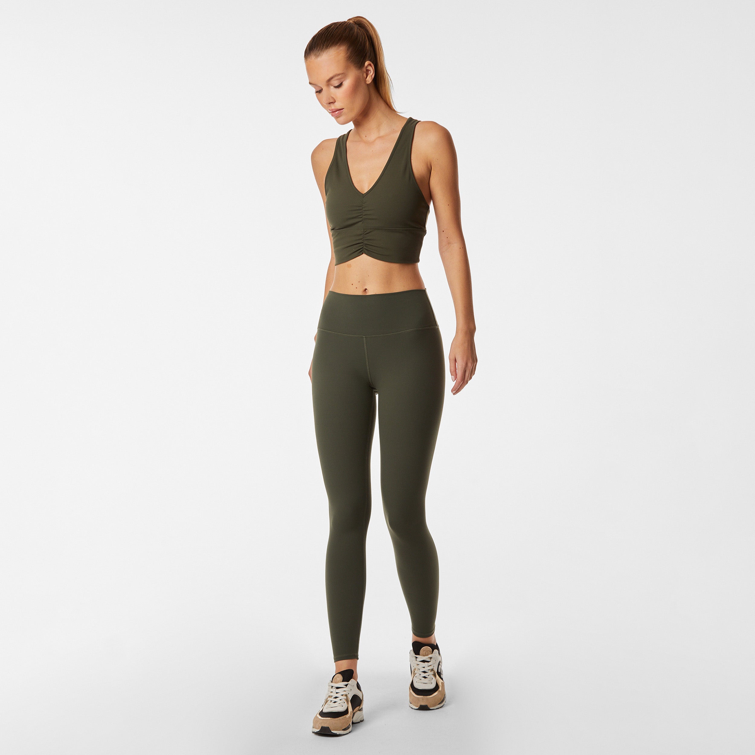 Full body view of woman wearing ruched front green racerback bra and matching legging