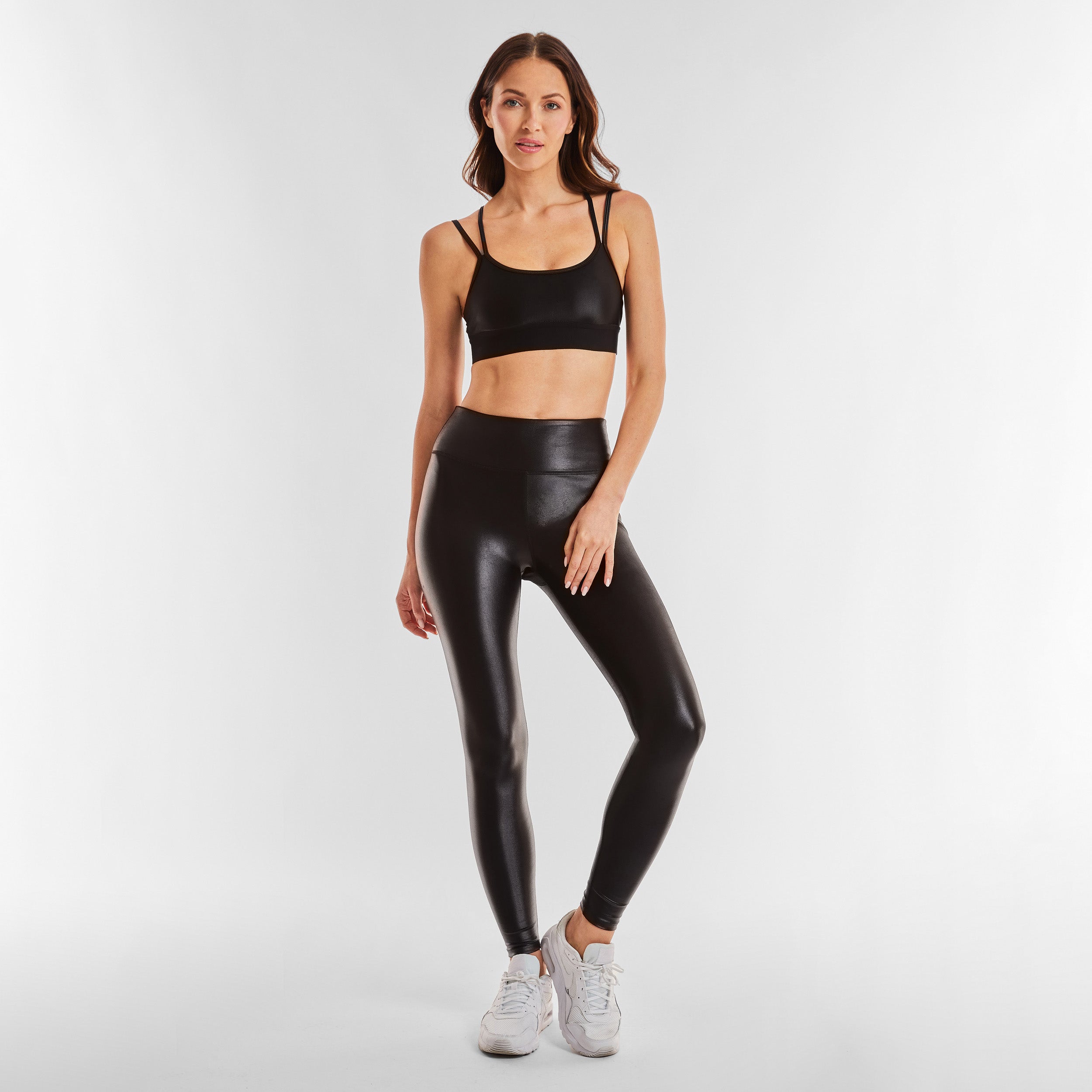 Full body view of woman wearing black gloss liquid sports bra featuring a scoop neckline and an alluring strappy back with a supportive elastic band