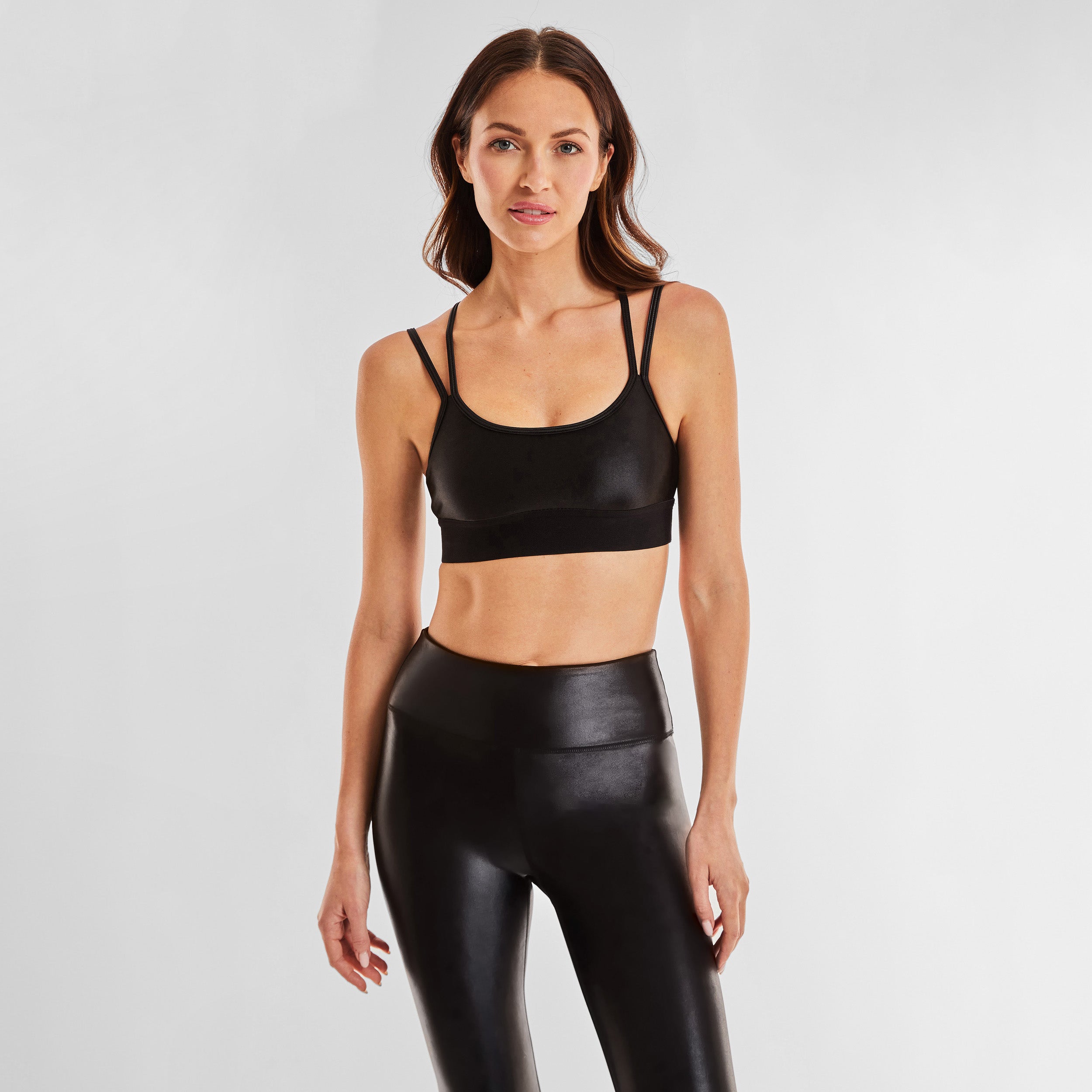 Front view of woman wearing black gloss liquid sports bra featuring a scoop neckline and an alluring strappy back with a supportive elastic band