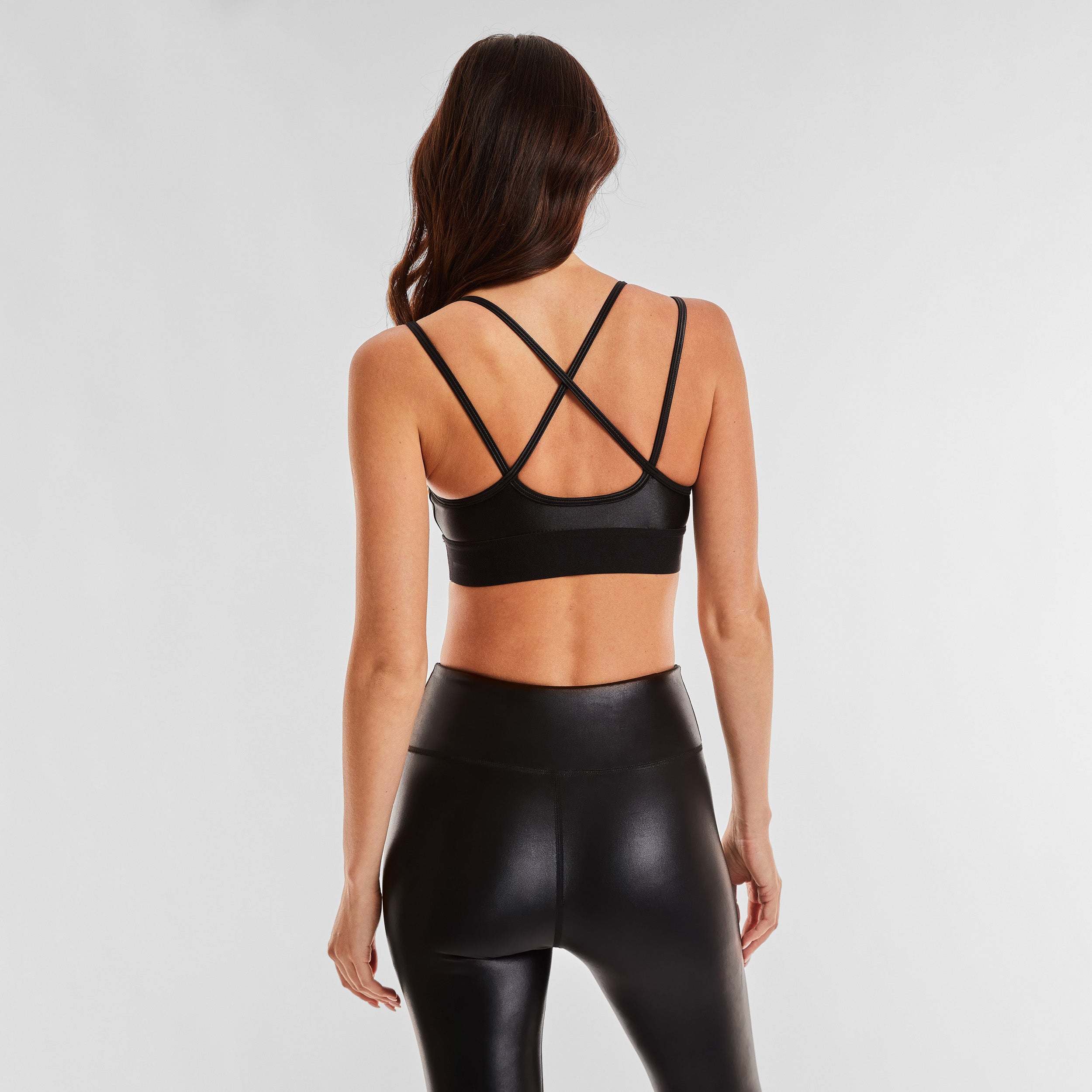 Rear view of woman wearing black gloss liquid sports bra featuring a scoop neckline and an alluring strappy back with a supportive elastic band