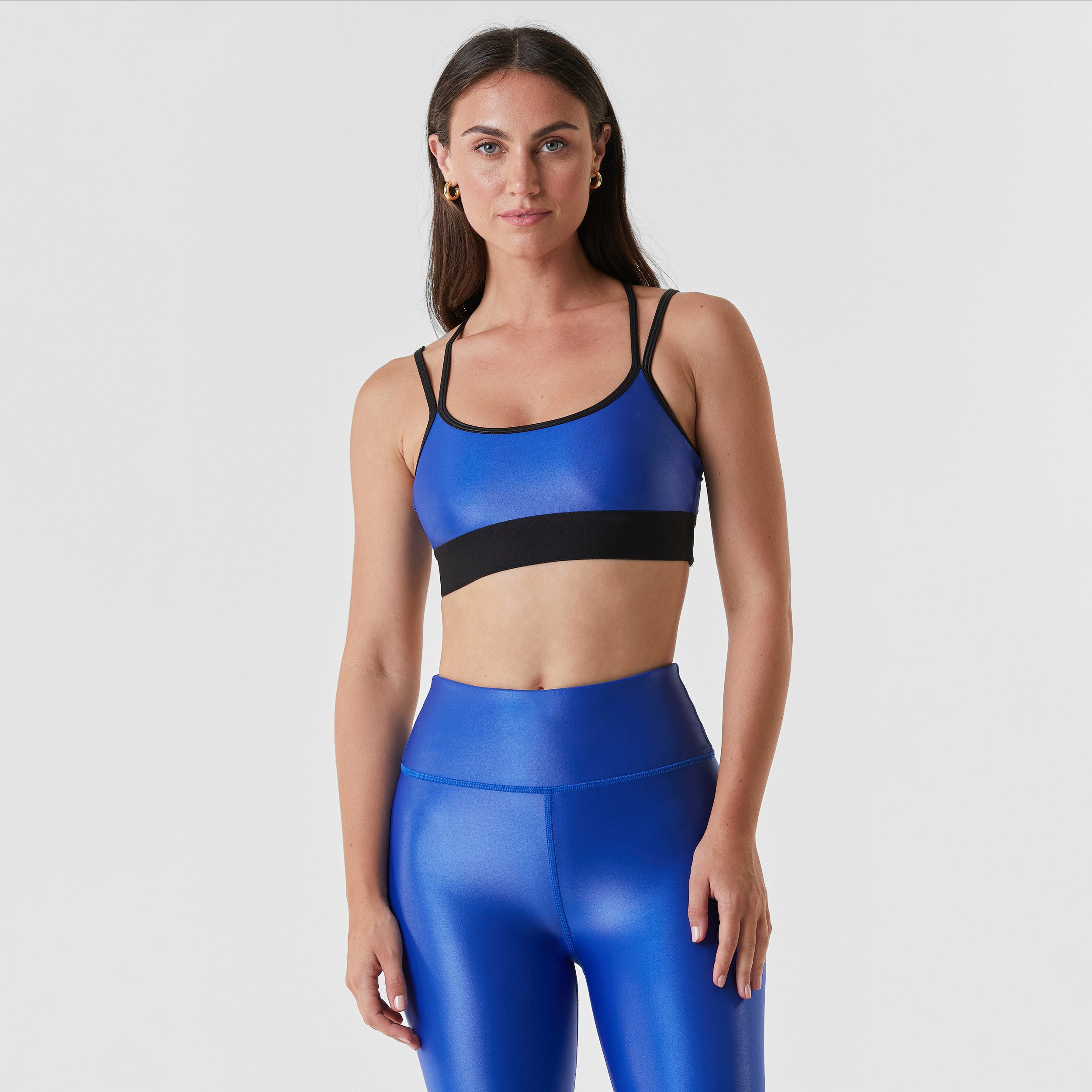 Front view of woman wearing cobalt blue gloss liquid sports bra featuring a scoop neckline and an alluring strappy back with a supportive elastic band