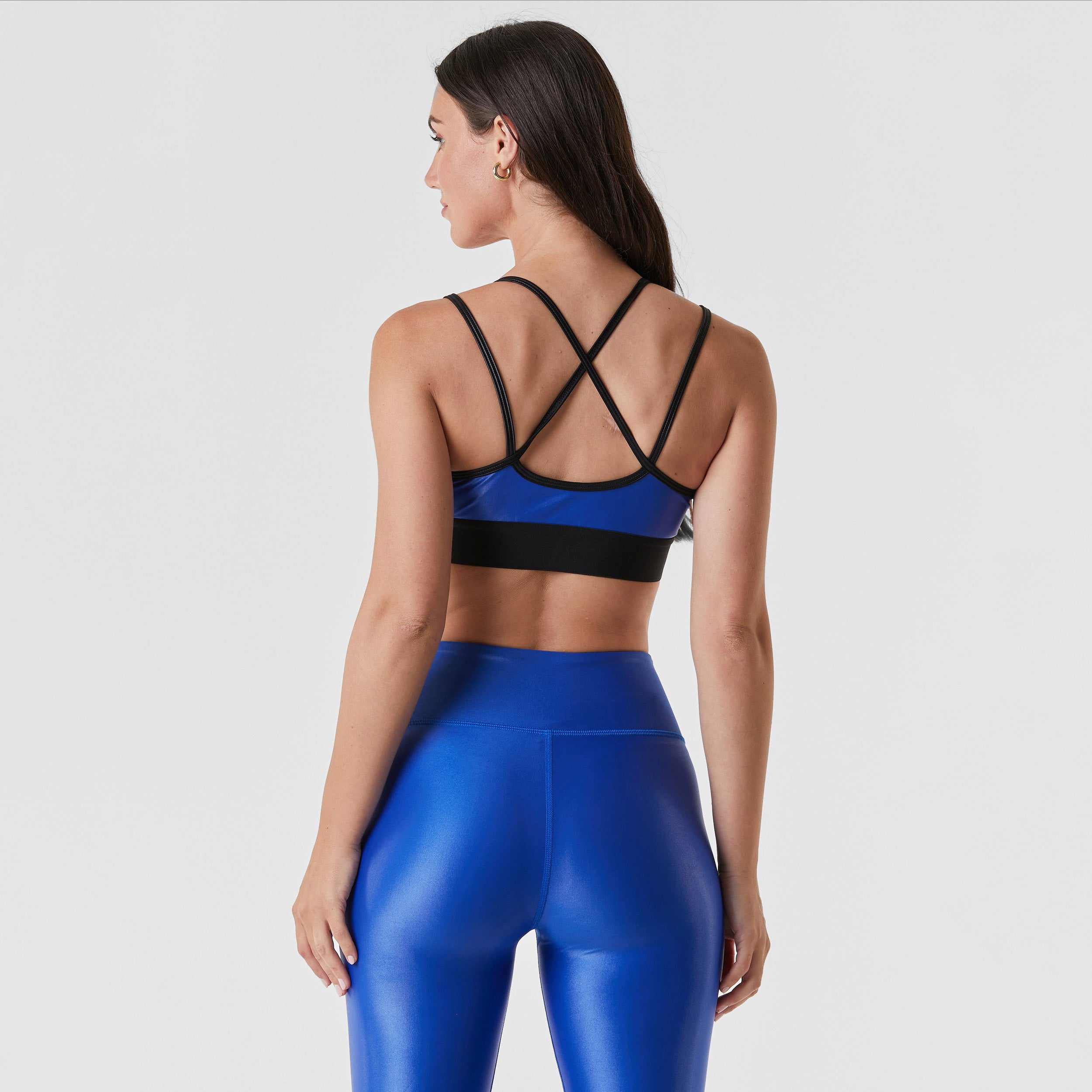 Rear view of woman wearing cobalt blue gloss liquid sports bra featuring a scoop neckline and an alluring strappy back with a supportive elastic band