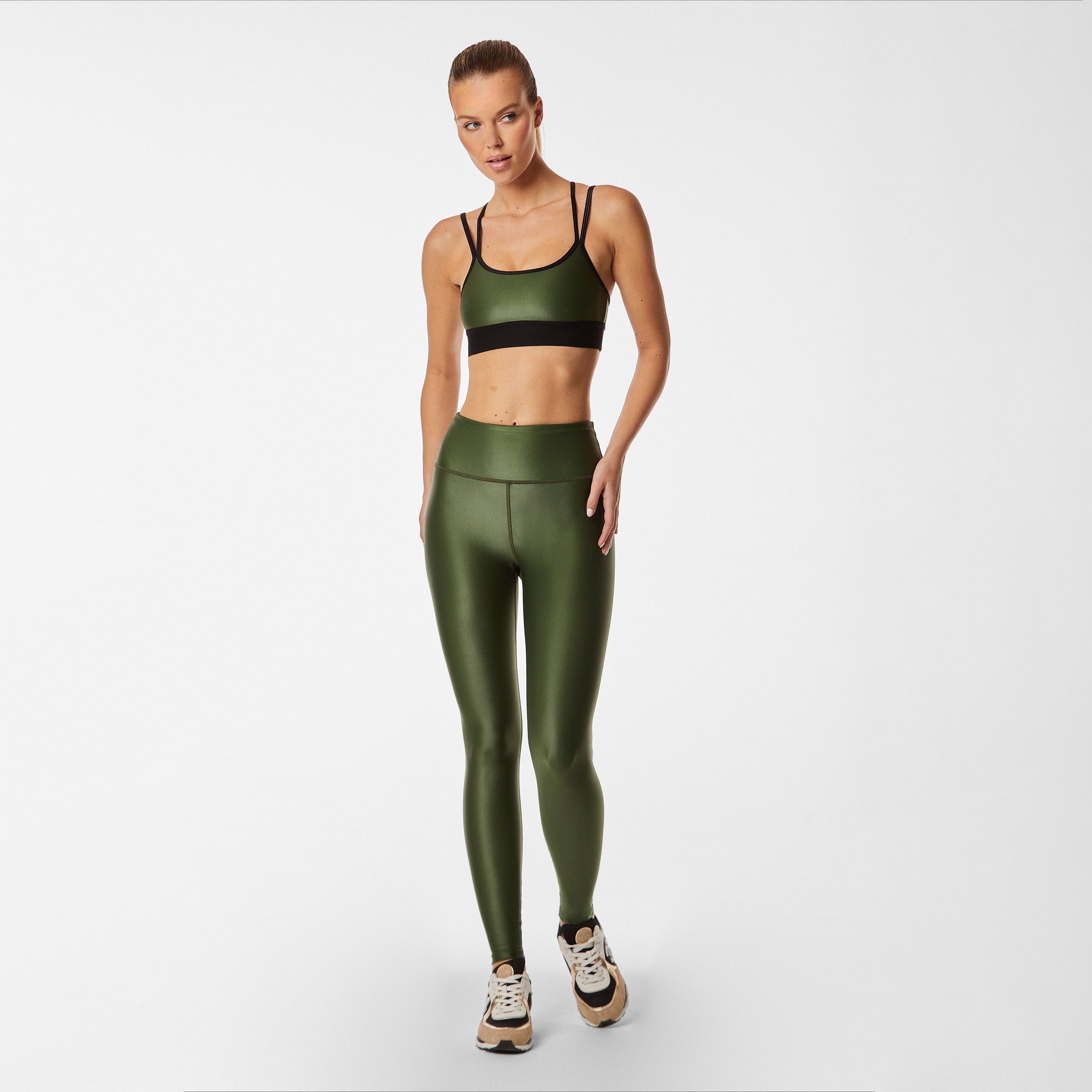 Full body view of woman wearing hunter green gloss liquid sports bra featuring a scoop neckline and an alluring strappy back with a supportive elastic band
