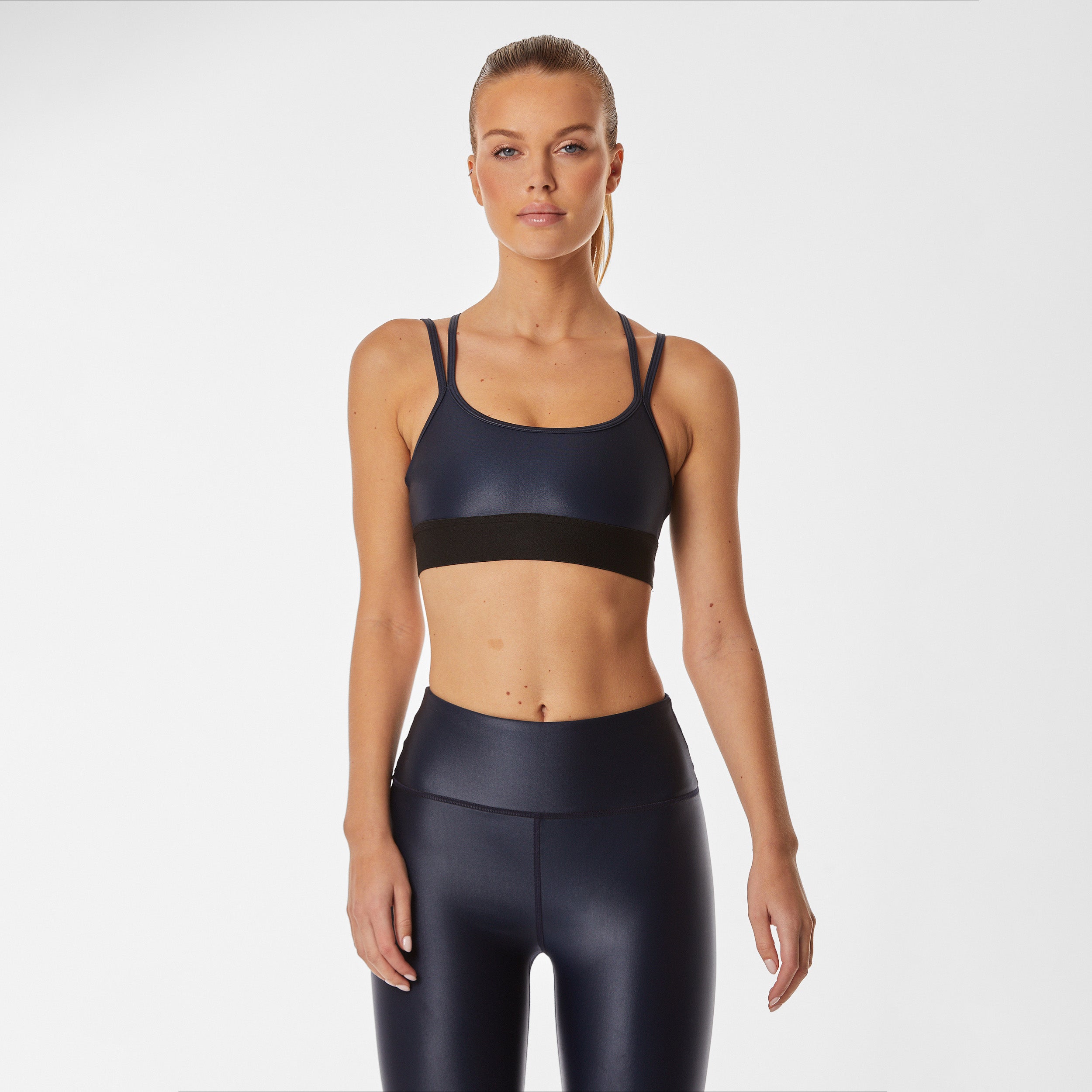 Front view of woman wearing navy blue gloss liquid sports bra featuring a scoop neckline and an alluring strappy back with a supportive elastic band