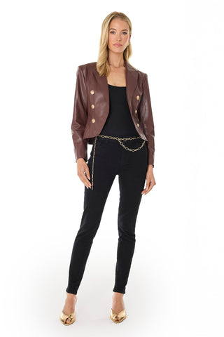 A woman with blonde hair and a neutral expression faces forward in the Gabrielle Leather Double Breasted Blazer - Espresso, featuring a tailored waist and gold buttons. She pairs it with a black top, black skinny jeans, gold chain belt, and gold heels.