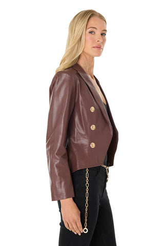 A woman with long blonde hair wears the Gabrielle Leather Double Breasted Blazer in Espresso, featuring gold buttons and a tailored waist, paired with black pants and a gold chain belt, shown in profile against a white background.
