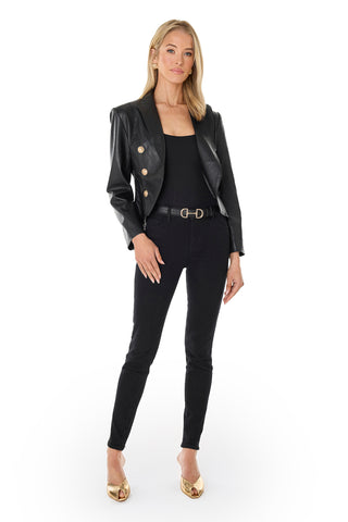 A woman with shoulder-length blonde hair poses against a white background in the Gabrielle Leather Double Breasted Blazer - Black with gold buttons, paired with a black top, black skinny pants, a gold-buckled belt, and gold open-toe heels.