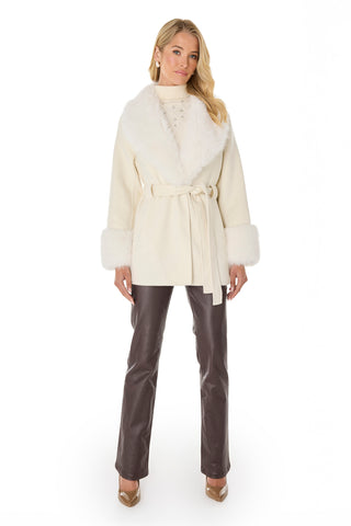A woman wears the Isabel Fur Trim Coat - White, featuring a white fur collar and cuffs, paired with brown leather pants and beige heels against a white background.