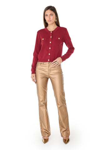 A woman faces forward wearing the Loretta Knit Cardigan Top in Merlot with gold dome buttons and pockets, paired with metallic gold straight-leg pants and gold pointed-toe heels against a plain white background.