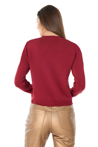 A woman with long brown hair wears gold hoop earrings and the Loretta Knit Cardigan Top in Merlot, paired with high-waisted tan leather pants, shown from the back against a white background.