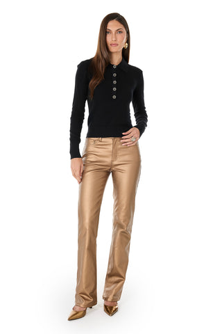 A woman with long brown hair and a neutral expression poses against a white background, wearing the Darla Rose Polo Shirt - Black with rose-shaped buttons, shiny gold pants, and gold pointed-toe heels.