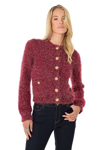 A woman with long blonde hair models the Joana Knit Cardigan in Merlot, featuring a textured, fuzzy knit and gold dome buttons. She pairs it with dark jeans and poses against a white background, one hand on her hip.