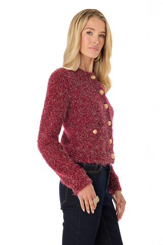 A woman stands confidently against a white background wearing the Joana Knit Cardigan in Merlot, featuring textured long sleeves and gold dome buttons, paired with dark jeans.