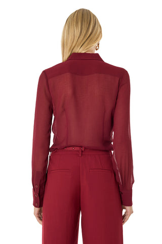 A woman with long blonde hair, seen from the back, wears a Georgia Semi-Sheer Blouse in burgundy with long sleeves and matching high-waisted red pants against a plain white background.