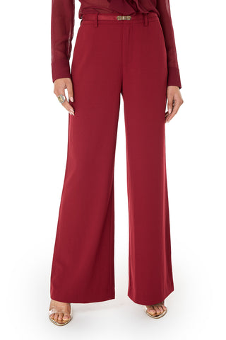 A person wearing the Martina Belted Trouser in Merlot, styled with a matching long-sleeve top, gold sandals, and a ring stands against a white background. The shot is cropped from the shoulders down.