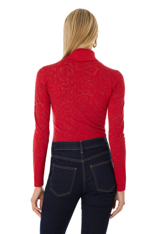A person with long blonde hair is shown from the back, wearing the slim-fitting Alina Rose Turtleneck Top in red and dark blue high-waisted jeans against a white background.