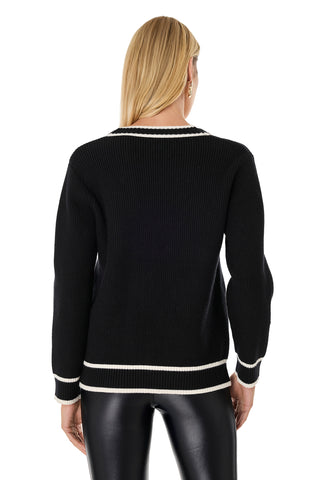 A person with straight blonde hair, seen from the back, wears the Devin Rose Contrast Cardigan - Black with white trim at the collar, cuffs, and hem, paired with shiny black pants.
