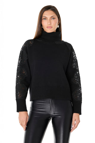 A woman wears the Camille Lace Turtleneck Sweater in black, featuring ultra-soft knit with lace details on the shoulders and sleeves, paired with black leather pants, against a white background.