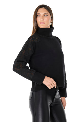 A woman models the Camille Lace Turtleneck Sweater in black, featuring delicate sleeve details, paired with black faux leather pants as she poses against a white background, looking to her left with one hand on her hip.