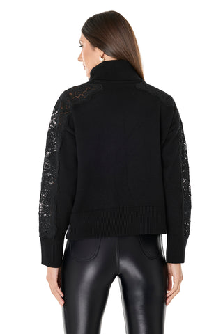A woman with long brown hair, seen from the back, wears the Camille Lace Turtleneck Sweater in black featuring delicate lace sleeves and pairs it with shiny black pants against a white background.