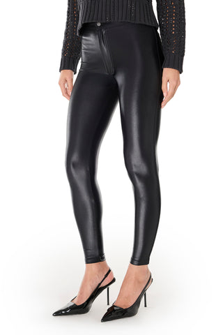 A person wearing Suzette Skinny Pant - Black with a high-rise waist, a textured black long-sleeve top, and black heels stands against a white background.